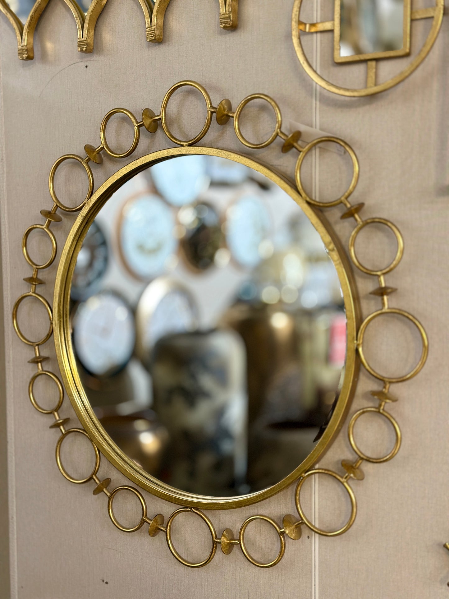 Decorative round gold metal wall mirror with interlocking ring frame design displayed at Fatima Home Decor store in Islamabad.