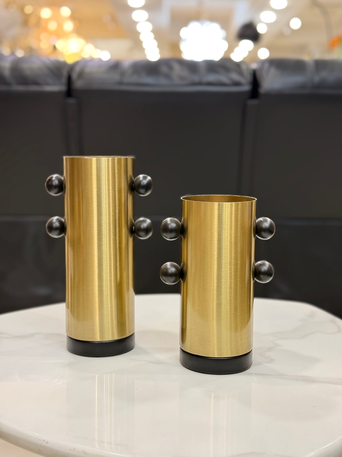 Set of two brushed gold metal vases with matte black spherical orbital accents and black bases at Fatima Home Décor store in Islamabad.