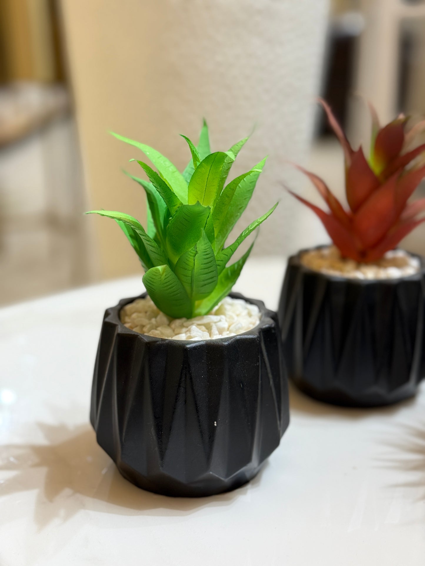 Artificial green agave succulent in a multi-faceted matte black geometric pot with white pebbles displayed at Fatima Home Décor store in Islamabad.
