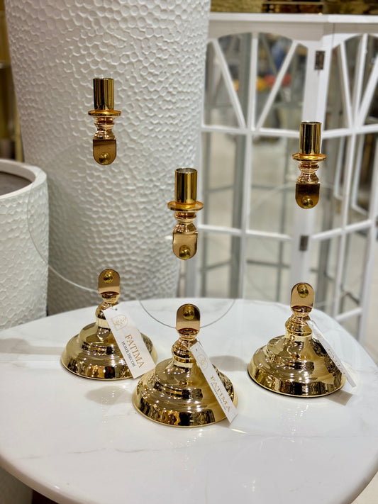 Set of three polished gold taper candle holders with bell-shaped bases and tiered stems at Fatima Home Decor store in Islamabad.