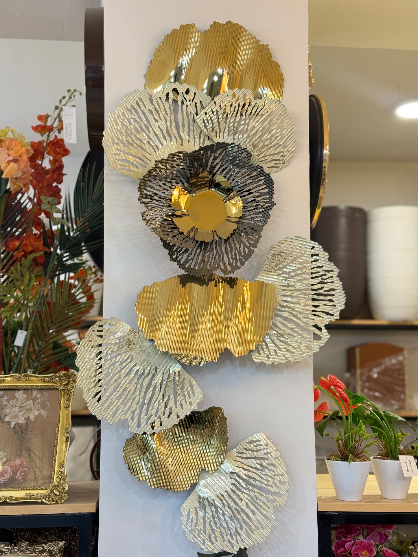 Vertical 3D gold metallic wall art featuring textured ginkgo-style leaves displayed on a white pillar at Fatima Home Décor store in Islamabad.