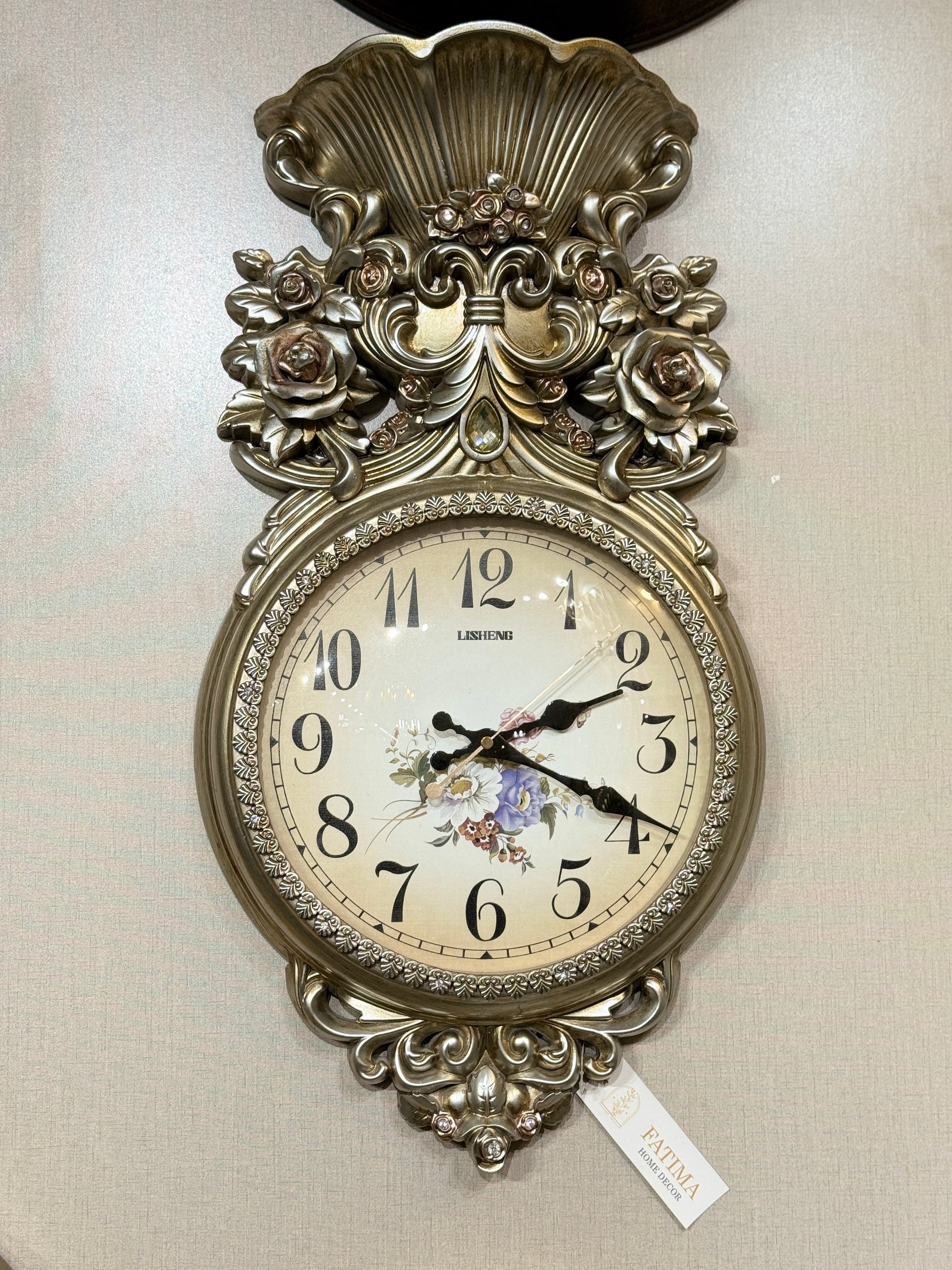 Ornate Lisheng champagne gold PVC wall clock with 3D rose carvings and floral dial displayed at Fatima Home Décor store in Islamabad.